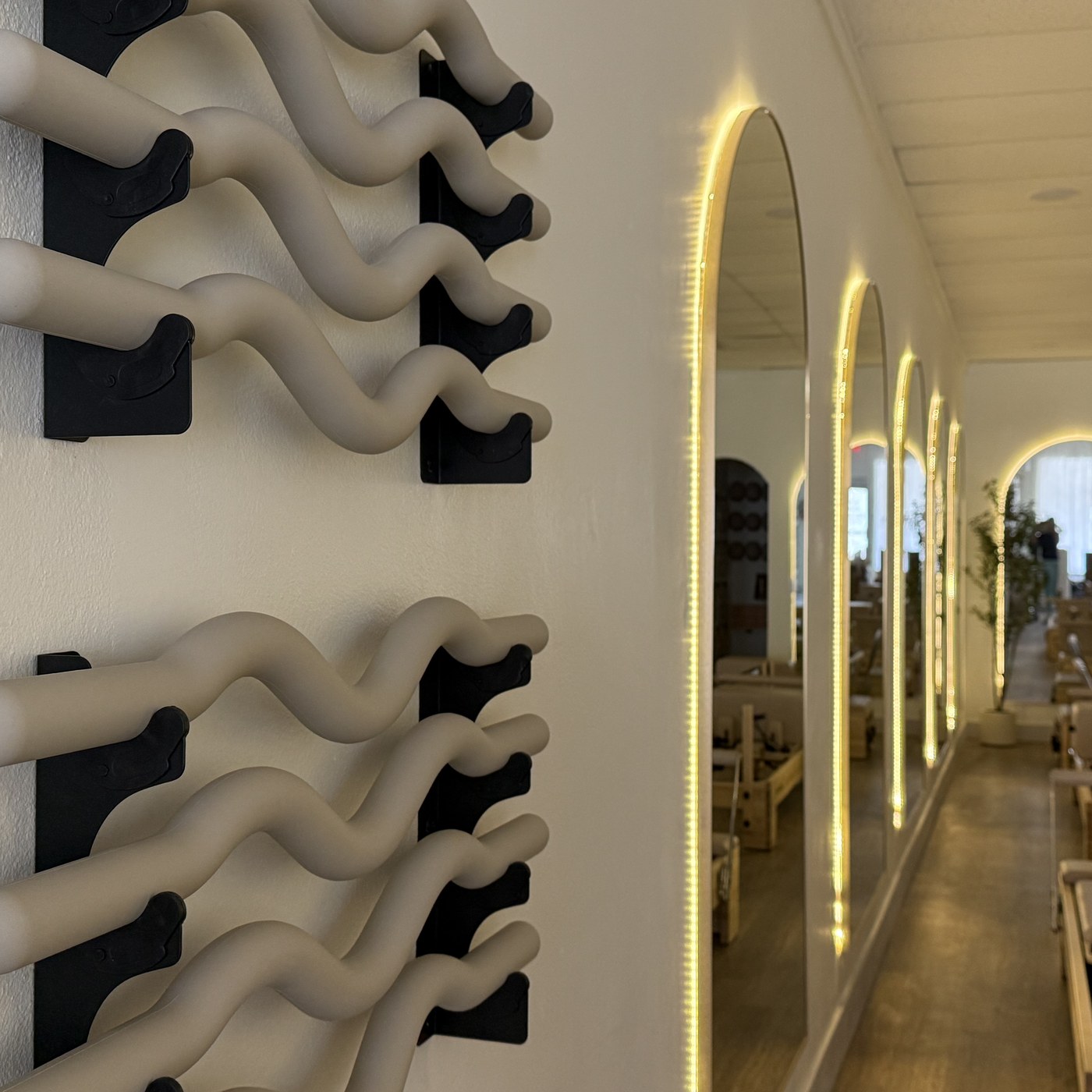 Wall-mounted Pilates props beside backlit arched mirrors in the MindFlow reformer studio